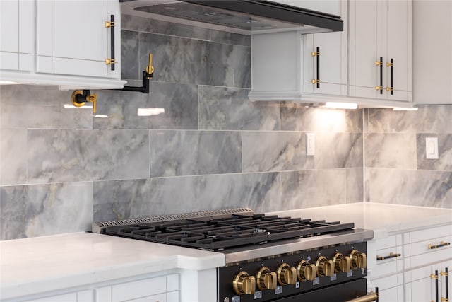 kitchen featuring gas range, backsplash, and white cabinets