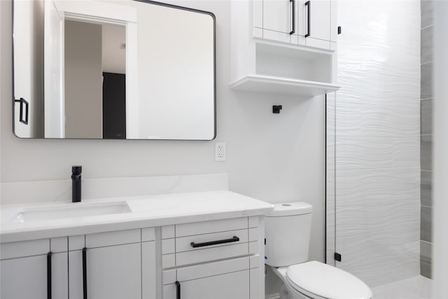 bathroom with toilet, a tile shower, and vanity