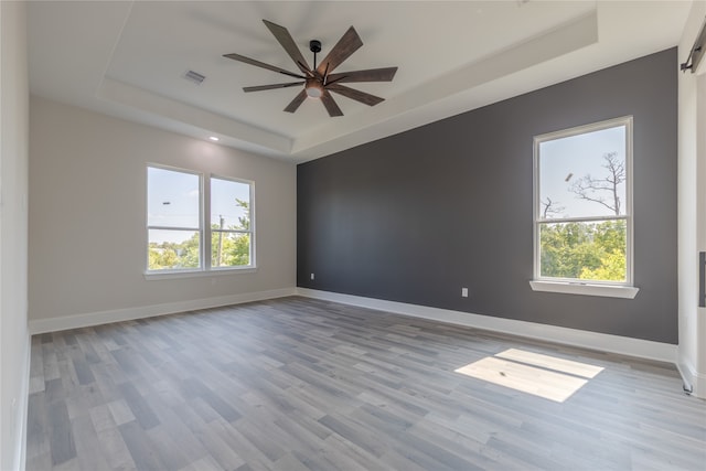 unfurnished room with ceiling fan, light wood-type flooring, and a tray ceiling