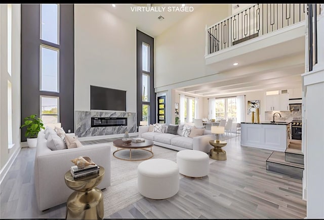 living room with wood-type flooring, a premium fireplace, a healthy amount of sunlight, and a high ceiling