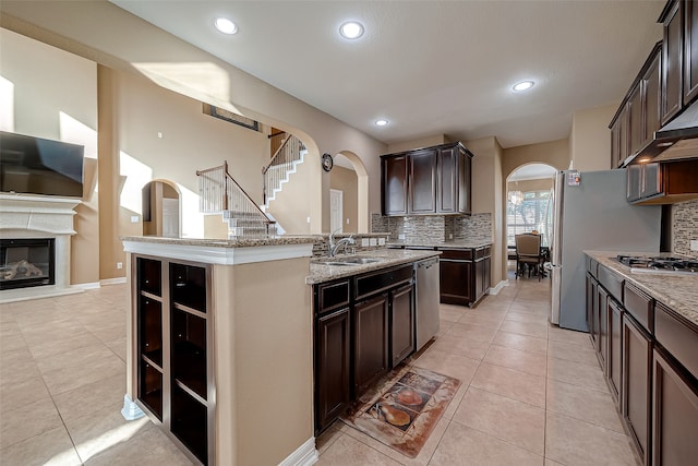 kitchen featuring appliances with stainless steel finishes, backsplash, dark brown cabinets, a center island with sink, and sink