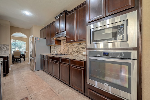 kitchen featuring dark brown cabinets, light stone countertops, stainless steel appliances, and light tile patterned floors