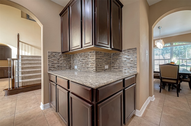 kitchen featuring dark brown cabinets, light stone counters, light tile patterned floors, and tasteful backsplash