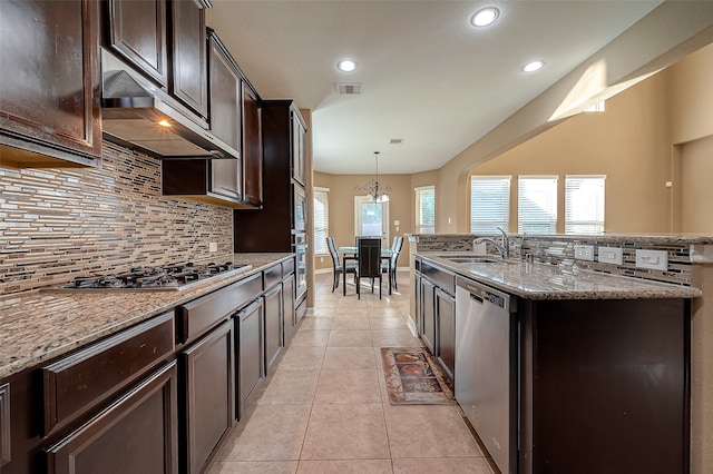 kitchen with light stone counters, a kitchen island with sink, tasteful backsplash, hanging light fixtures, and appliances with stainless steel finishes