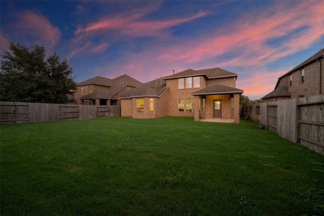 back house at dusk featuring a lawn and a patio