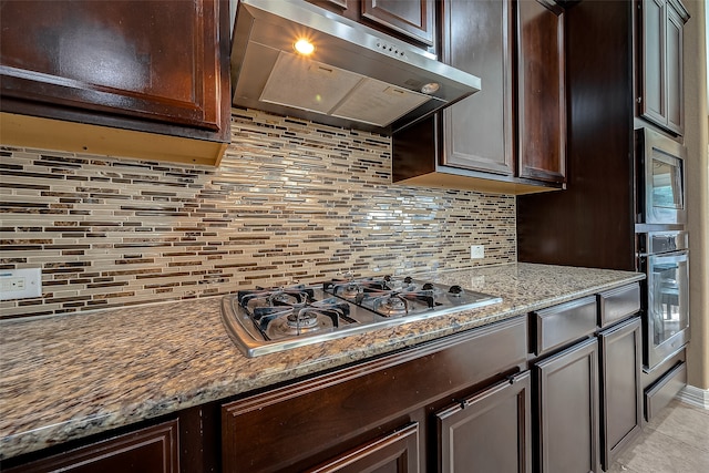 kitchen with tasteful backsplash, dark brown cabinets, stone counters, exhaust hood, and stainless steel appliances