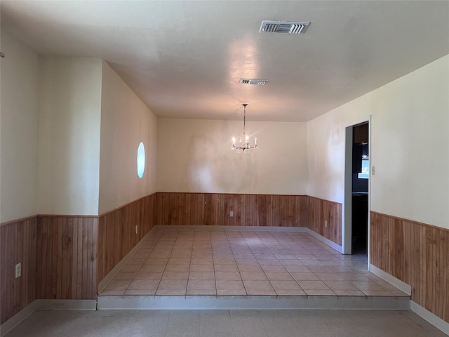 tiled spare room featuring wooden walls and a chandelier