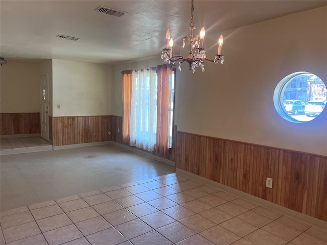 tiled spare room featuring wooden walls and a chandelier