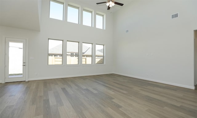 unfurnished living room featuring ceiling fan, hardwood / wood-style floors, and a towering ceiling