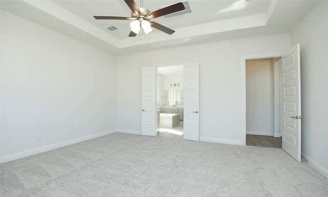 unfurnished bedroom featuring connected bathroom, a tray ceiling, ceiling fan, and light colored carpet