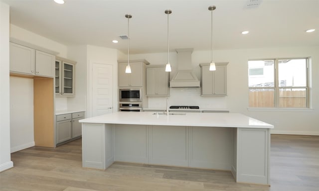 kitchen featuring pendant lighting, custom range hood, an island with sink, and appliances with stainless steel finishes