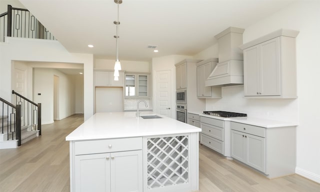 kitchen featuring sink, stainless steel appliances, premium range hood, an island with sink, and pendant lighting