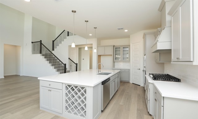 kitchen with decorative backsplash, stainless steel dishwasher, hanging light fixtures, white gas stove, and an island with sink