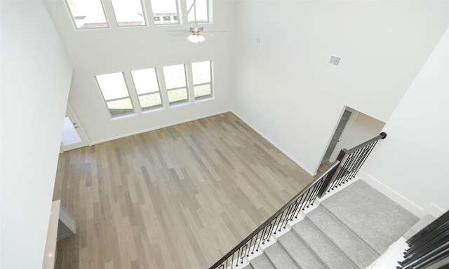 unfurnished living room featuring ceiling fan, a towering ceiling, and light hardwood / wood-style floors