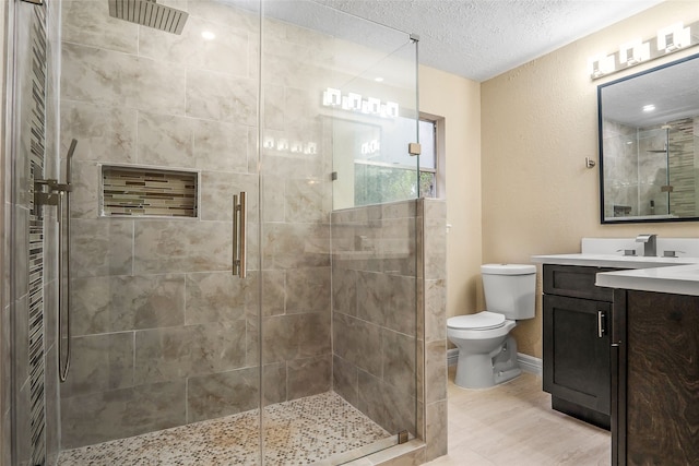 bathroom featuring vanity, toilet, a shower with door, and a textured ceiling