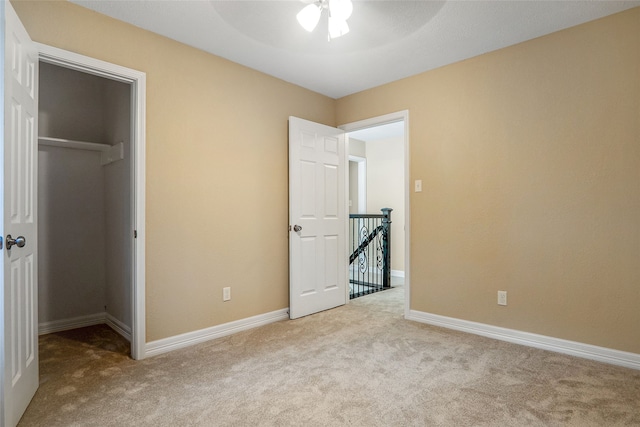 unfurnished bedroom featuring a walk in closet, light colored carpet, a closet, and ceiling fan