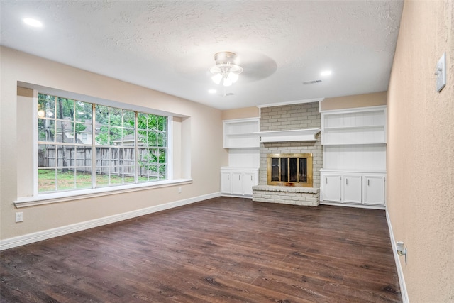 unfurnished living room featuring a fireplace, ceiling fan, brick wall, a textured ceiling, and dark wood-type flooring