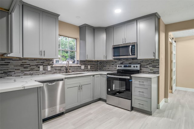 kitchen with tasteful backsplash, light stone countertops, appliances with stainless steel finishes, and gray cabinetry