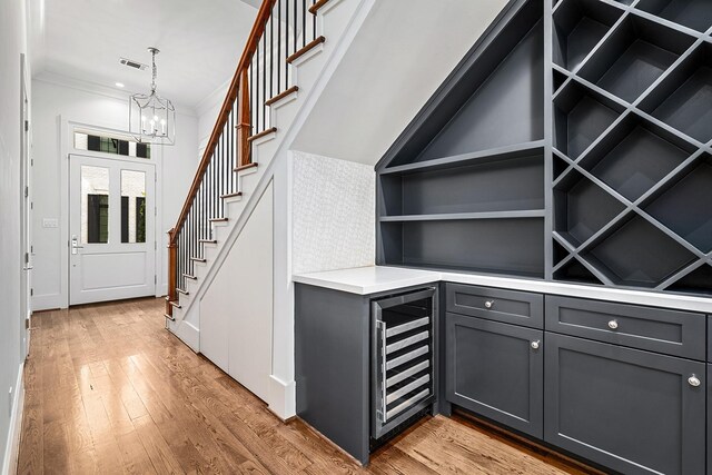 interior space with beverage cooler, a chandelier, light wood-type flooring, and crown molding