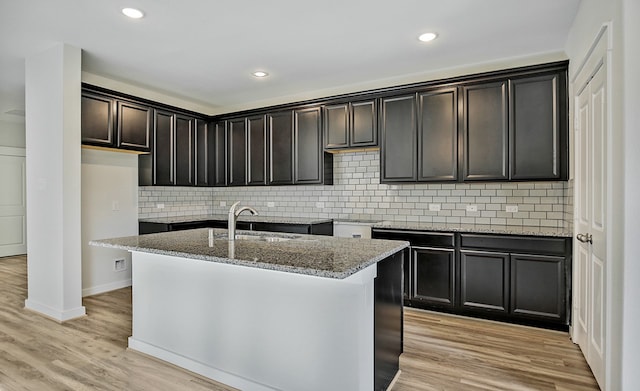 kitchen featuring decorative backsplash, light hardwood / wood-style floors, a kitchen island with sink, and sink