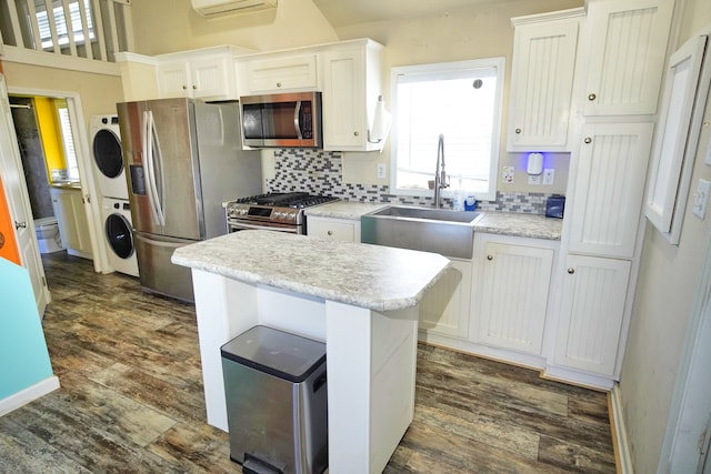 kitchen featuring stainless steel appliances, white cabinets, stacked washing maching and dryer, and sink