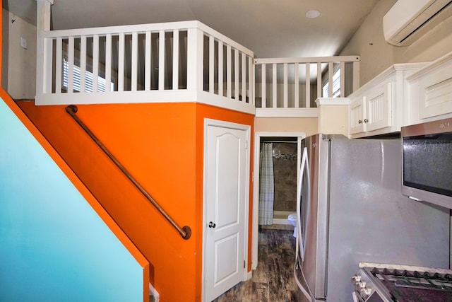 kitchen with appliances with stainless steel finishes, a wall mounted air conditioner, dark hardwood / wood-style flooring, and white cabinetry