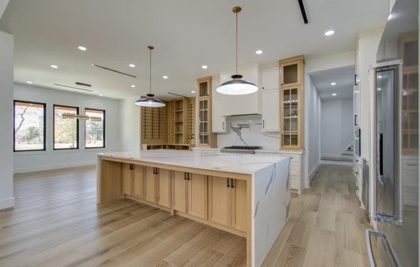 kitchen with a large island, light stone counters, light hardwood / wood-style flooring, and pendant lighting