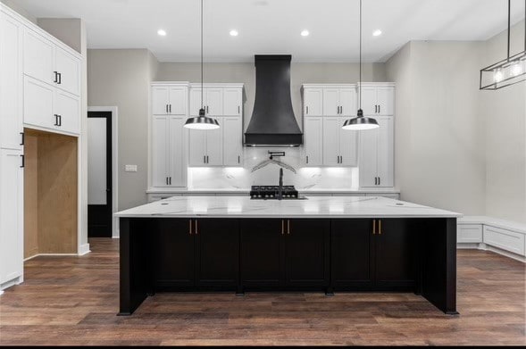 kitchen with a spacious island, white cabinets, custom range hood, and decorative light fixtures