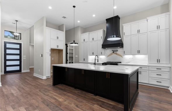 kitchen featuring dark hardwood / wood-style flooring, custom exhaust hood, an island with sink, and white cabinets