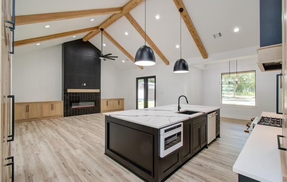 kitchen with stainless steel appliances, beamed ceiling, pendant lighting, and a center island with sink