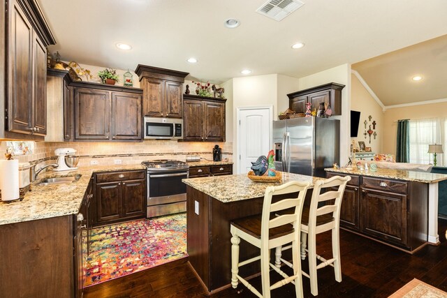 kitchen with dark brown cabinets, dark hardwood / wood-style floors, light stone countertops, appliances with stainless steel finishes, and decorative backsplash