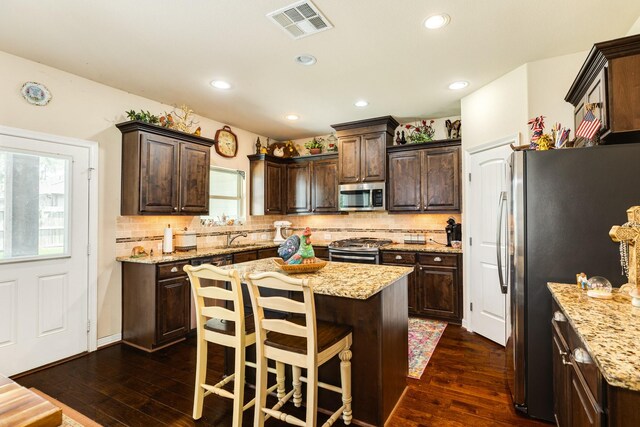 kitchen with tasteful backsplash, dark hardwood / wood-style flooring, light stone countertops, a kitchen island, and appliances with stainless steel finishes