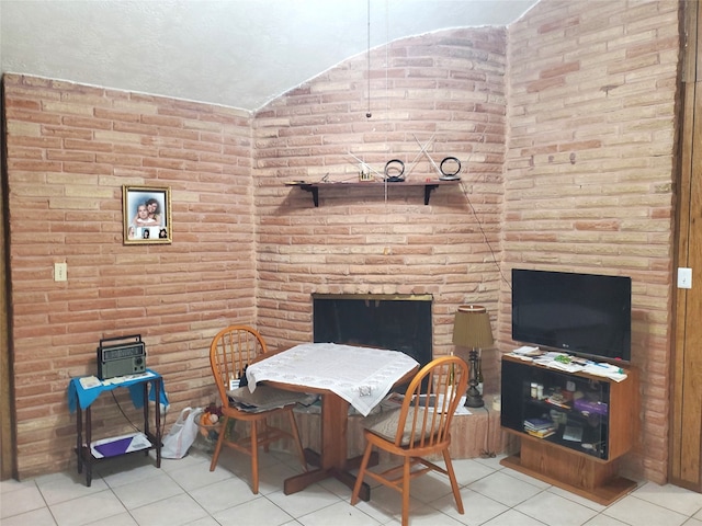 tiled dining area with brick wall, a fireplace, and lofted ceiling