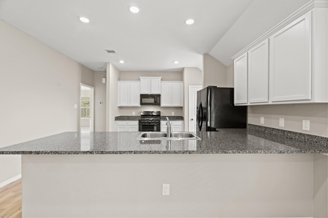 kitchen featuring dark stone counters, a peninsula, black appliances, white cabinetry, and a sink