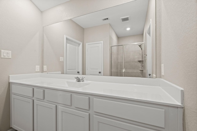 full bathroom featuring a textured wall, vanity, a shower stall, and visible vents