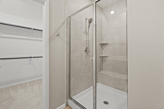 full bathroom featuring a stall shower, a walk in closet, and a textured wall