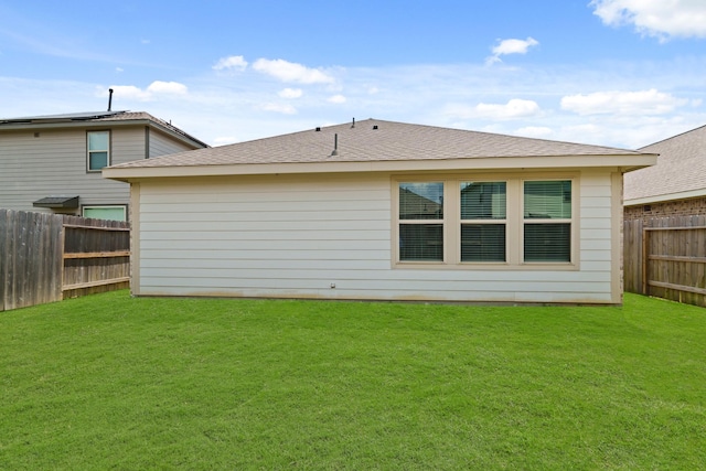 rear view of property featuring a yard, roof with shingles, and a fenced backyard