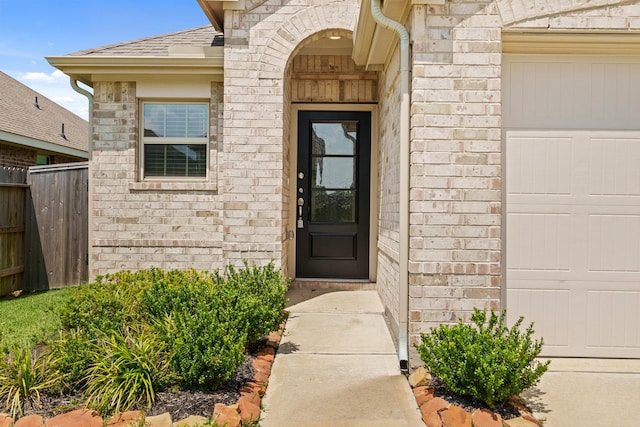 doorway to property with a garage, brick siding, fence, and roof with shingles