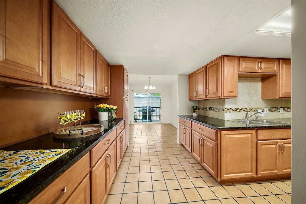 kitchen with light tile patterned flooring, dark stone countertops, tasteful backsplash, an inviting chandelier, and a textured ceiling