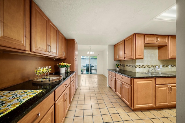 kitchen with light tile patterned flooring, dark stone countertops, tasteful backsplash, an inviting chandelier, and a textured ceiling