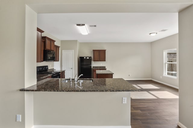 kitchen with black appliances, dark hardwood / wood-style flooring, sink, dark stone countertops, and kitchen peninsula