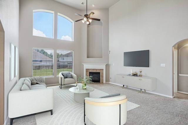 carpeted living room featuring a towering ceiling, a tiled fireplace, and ceiling fan