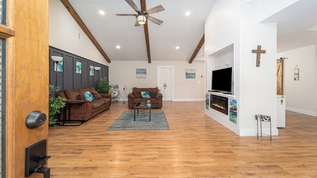 living room featuring beamed ceiling, light hardwood / wood-style floors, a large fireplace, and ceiling fan