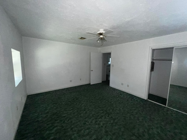 unfurnished bedroom featuring a textured ceiling, visible vents, a ceiling fan, a closet, and dark colored carpet