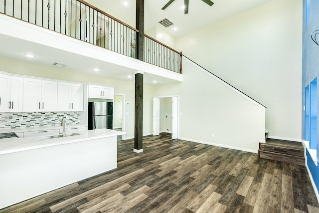 unfurnished living room with ceiling fan, sink, dark hardwood / wood-style flooring, and a towering ceiling