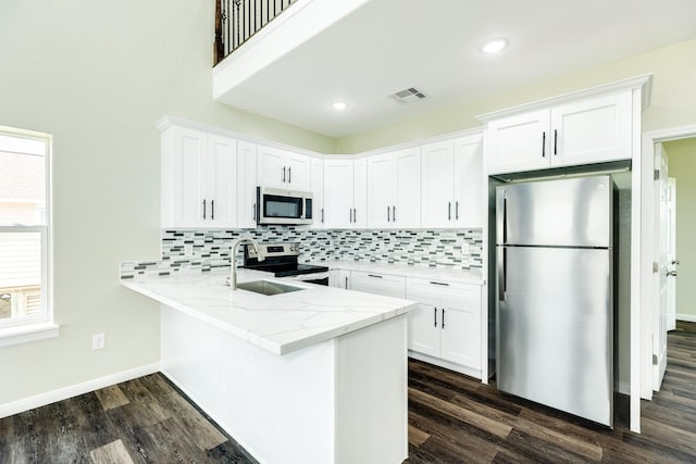 kitchen featuring appliances with stainless steel finishes, white cabinets, kitchen peninsula, light stone countertops, and dark wood-type flooring