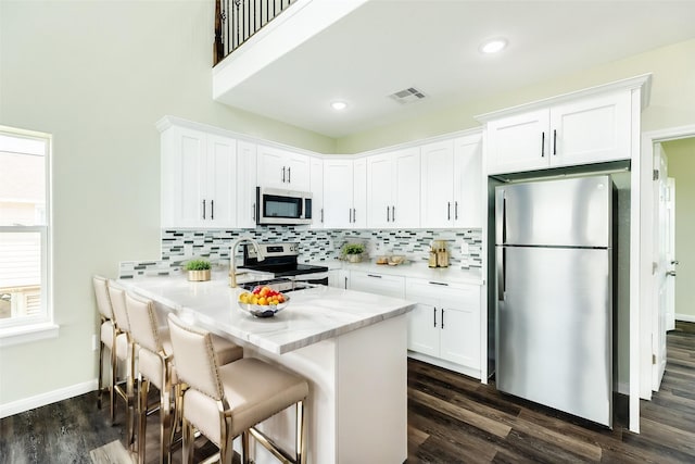 kitchen featuring a breakfast bar area, white cabinetry, stainless steel appliances, decorative backsplash, and kitchen peninsula