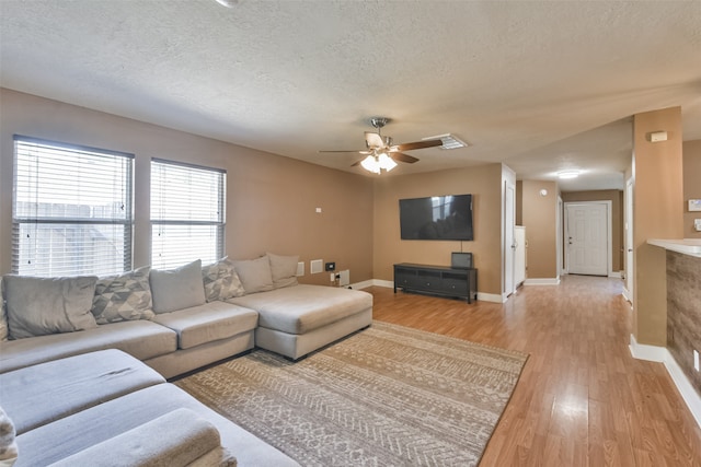 living room featuring ceiling fan, light hardwood / wood-style flooring, and a textured ceiling