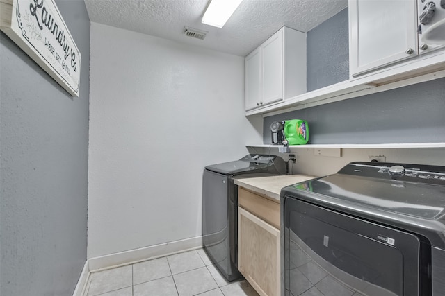 laundry area with light tile patterned floors, cabinets, a textured ceiling, and washer and clothes dryer