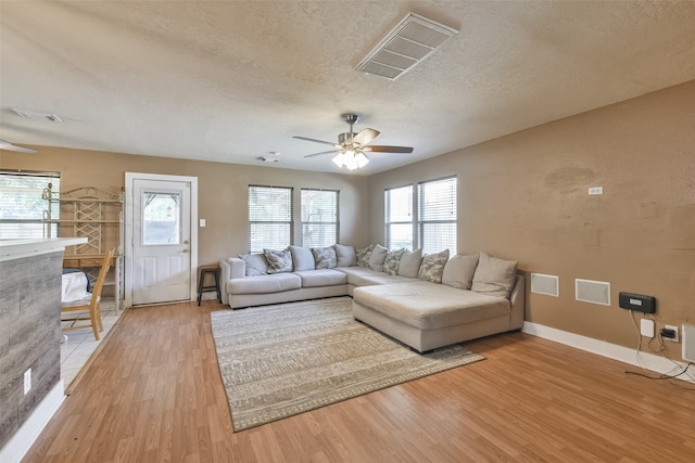 living room featuring ceiling fan, light hardwood / wood-style flooring, and a textured ceiling